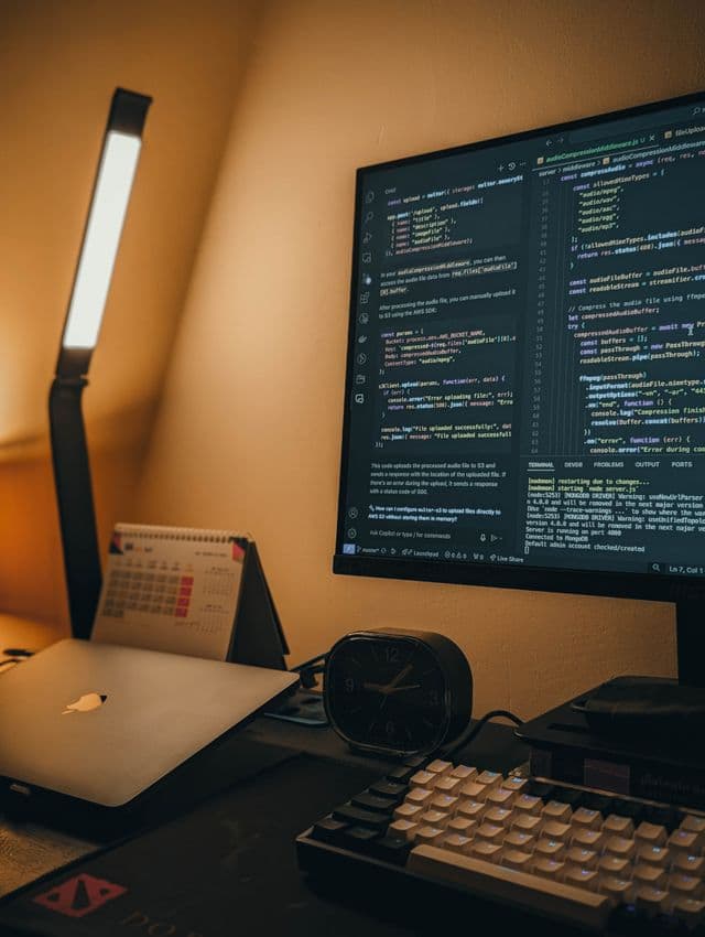 Monitor showing code beside a keyboard and desk lamp
